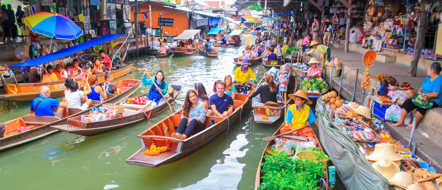 Tourists and vendors in traditional boats navigate the bustling Amphawa Floating Market in Thailand.