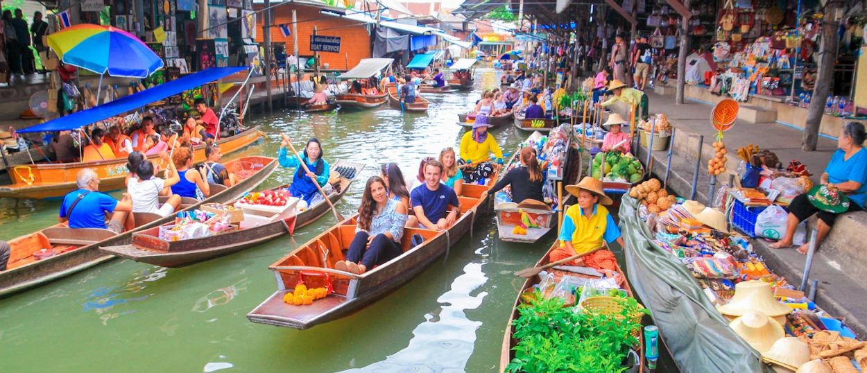 Tourists and vendors in traditional boats navigate the bustling Amphawa Floating Market in Thailand.