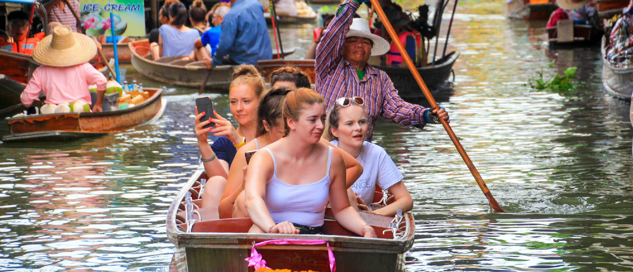 Young women enjoy a boat ride through the lively Amphawa Floating Market in Thailand.