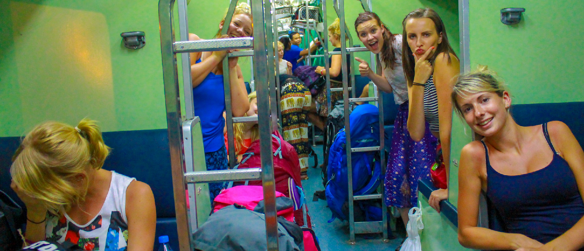 Young women travelers smiling and posing inside a lively overnight train in Thailand.
