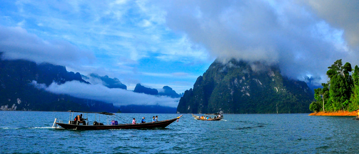 Longtail boats carry tourists across Cheow Lan Lake, surrounded by misty limestone mountains in Khao Sok National Park.