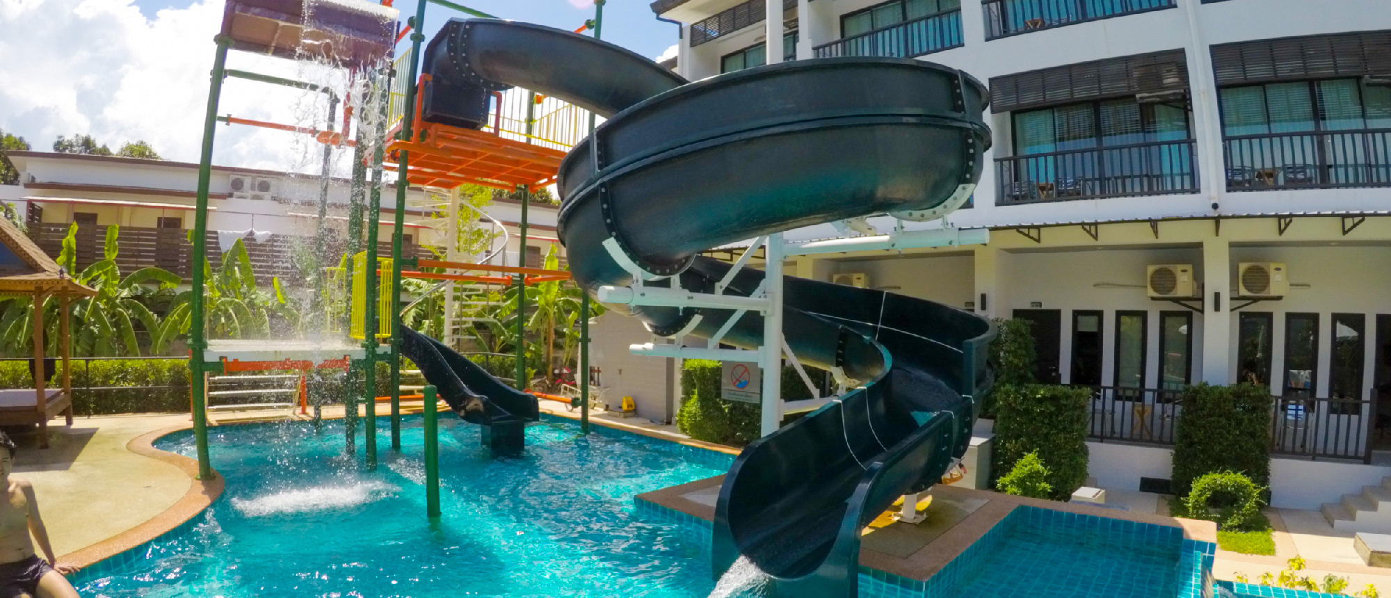 A resort swimming pool with a large black spiral water slide and splash area in Krabi.