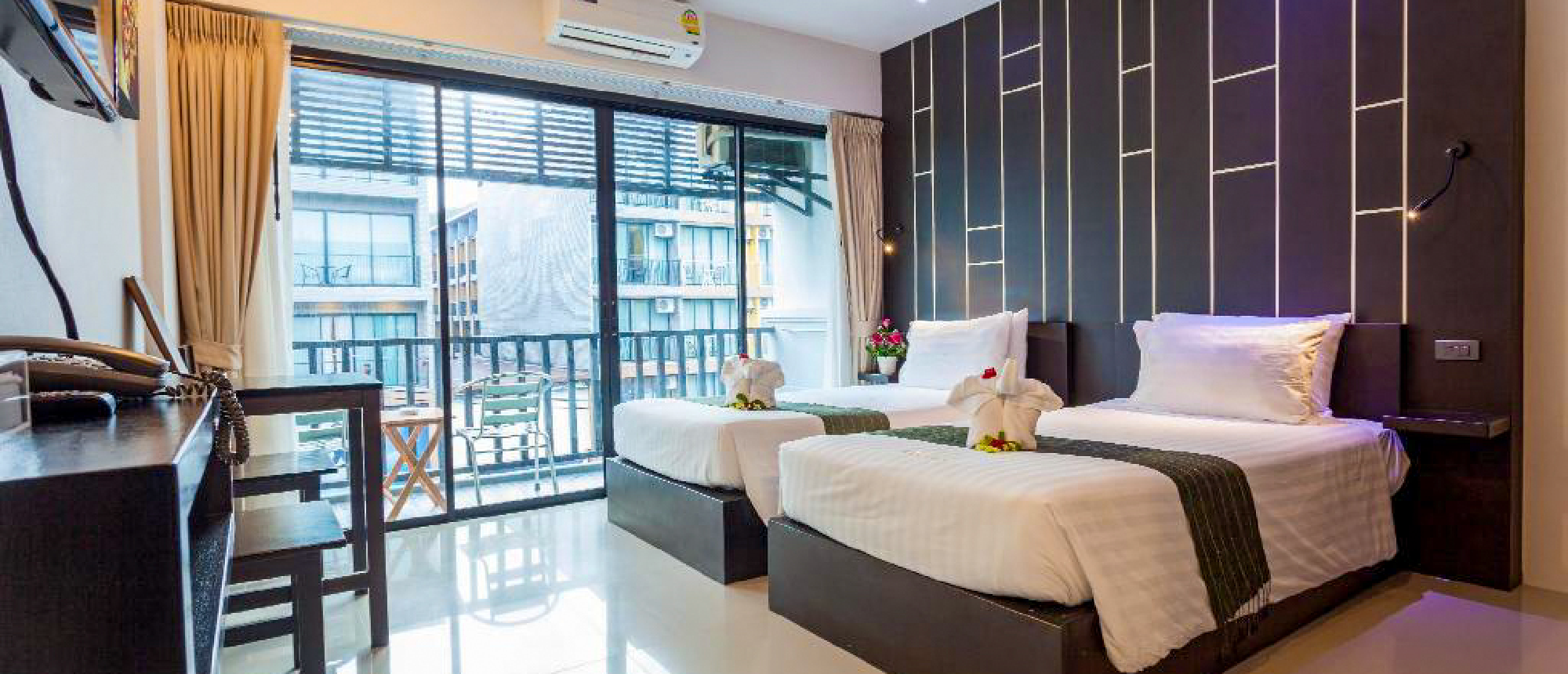 Inviting modern hotel room with two single beds, decorative towels, and a balcony in Krabi.