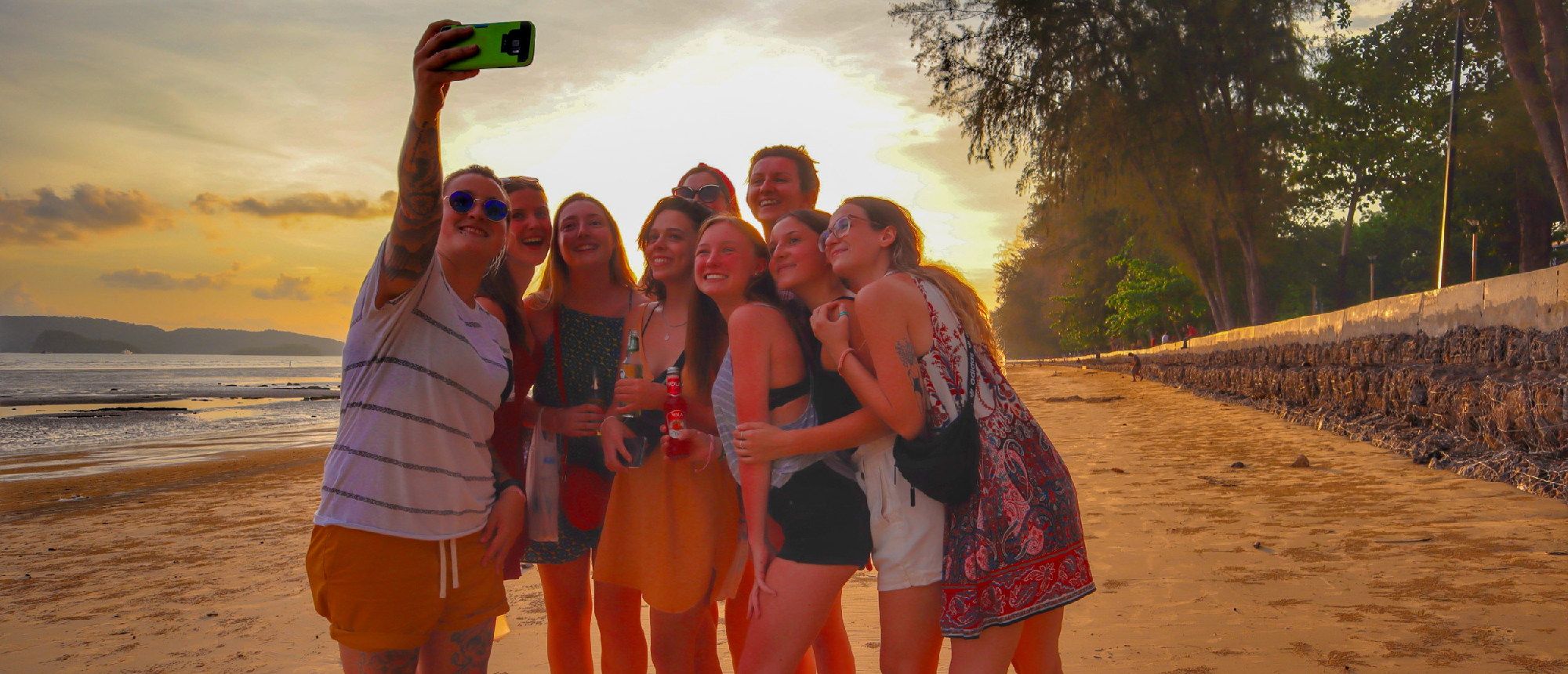 A group of joyful friends taking a selfie on a sandy beach at sunset in Krabi.