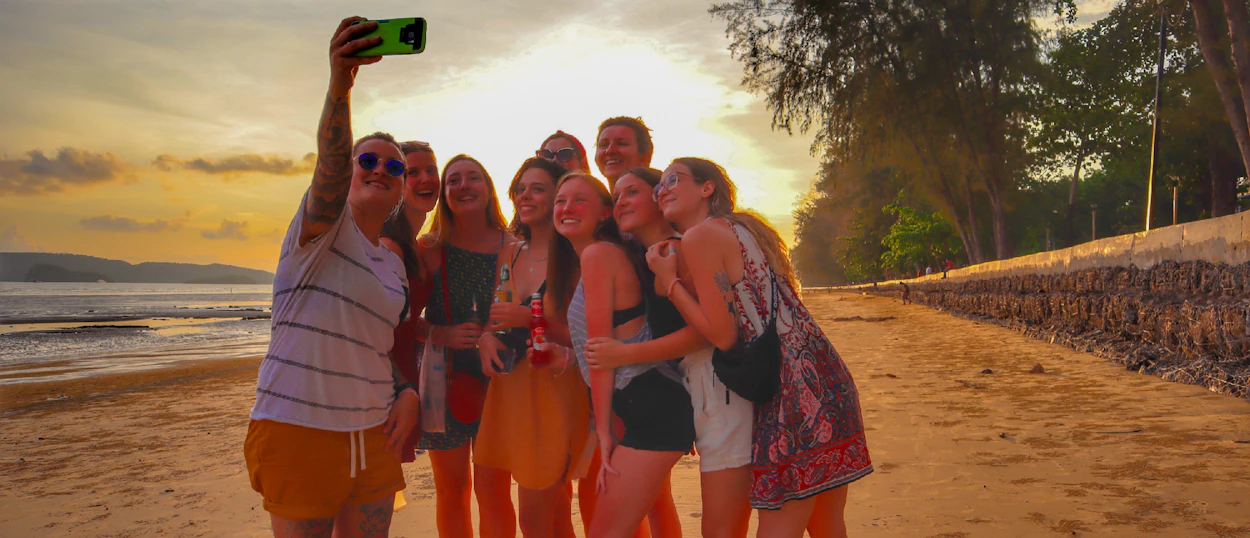 A group of joyful friends taking a selfie on a sandy beach at sunset in Krabi.