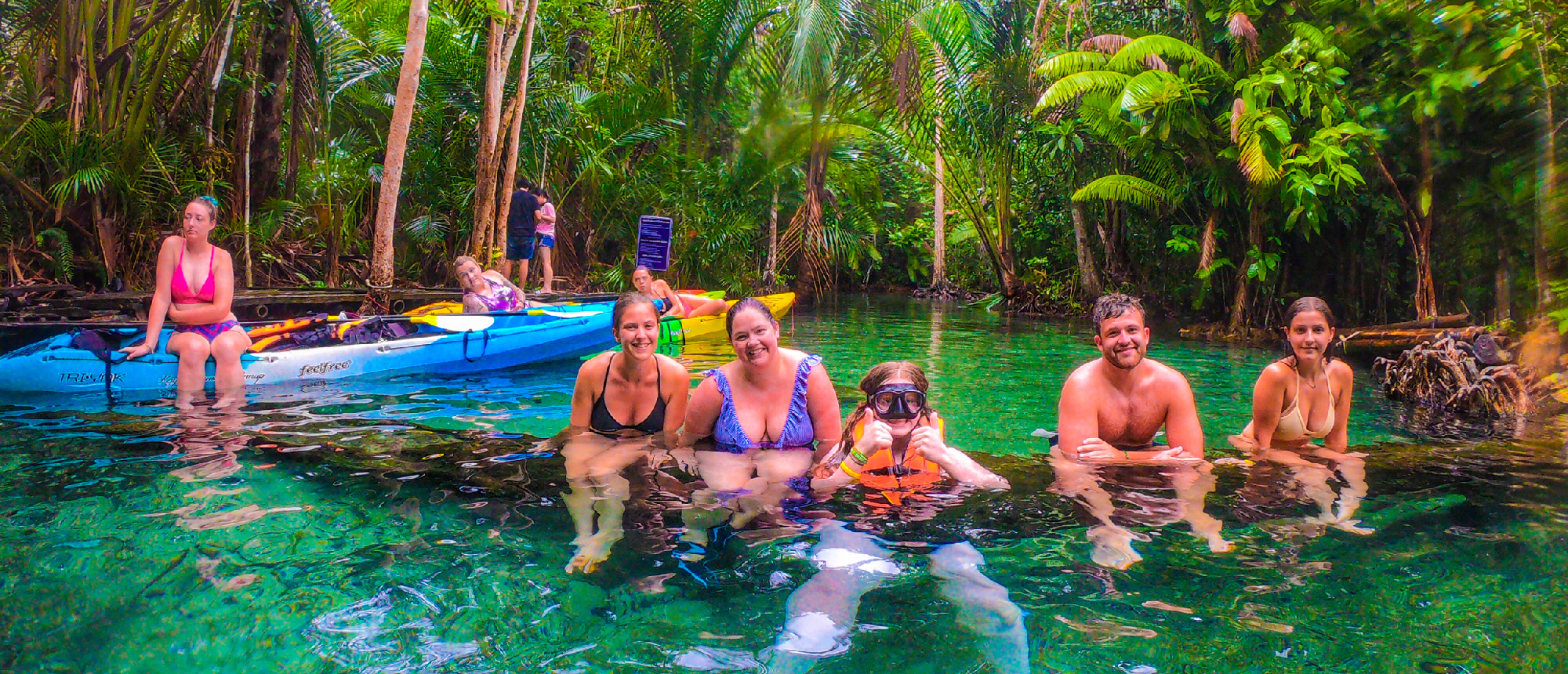 Smiling people enjoy a refreshing swim in the clear, emerald river surrounded by lush jungle in Krabi.