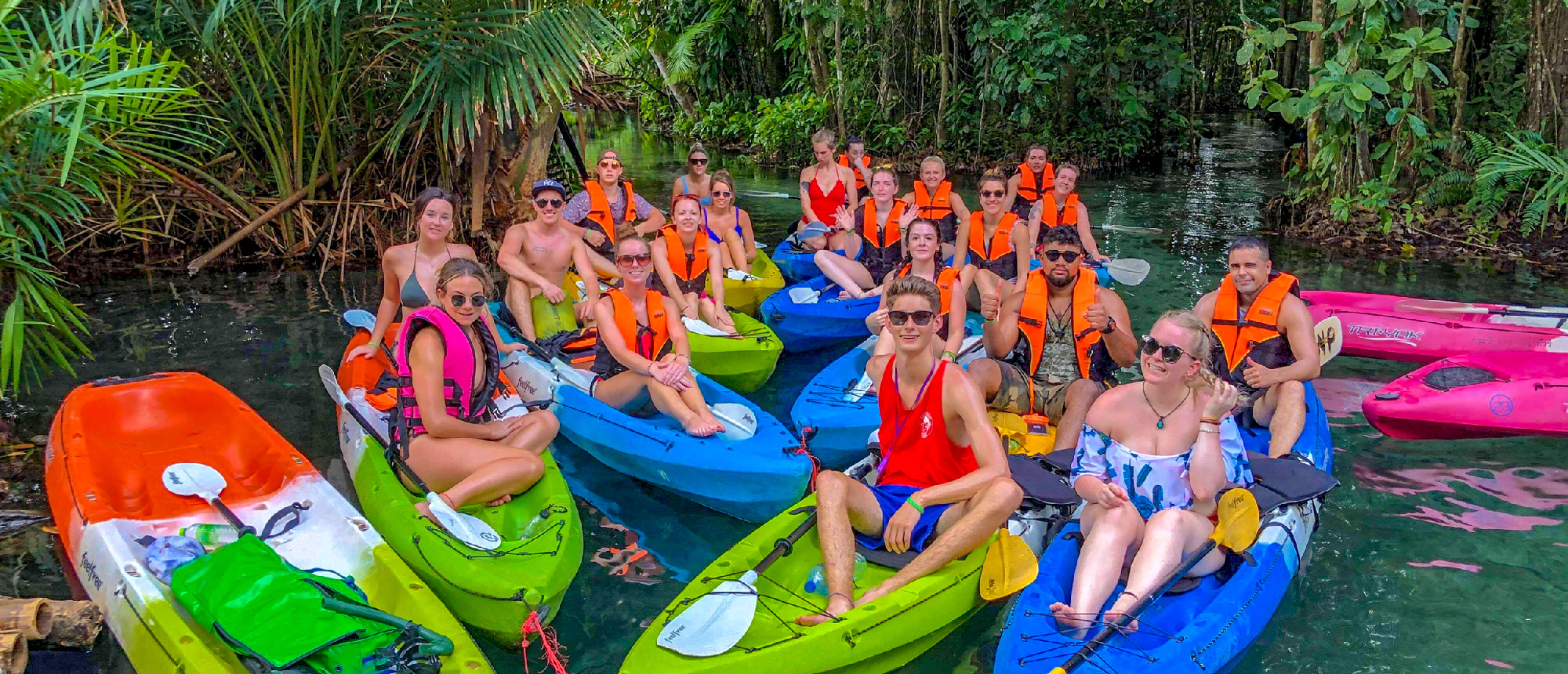 Smiling tourists in colorful kayaks paddle on a clear emerald river surrounded by lush jungle in Krabi.