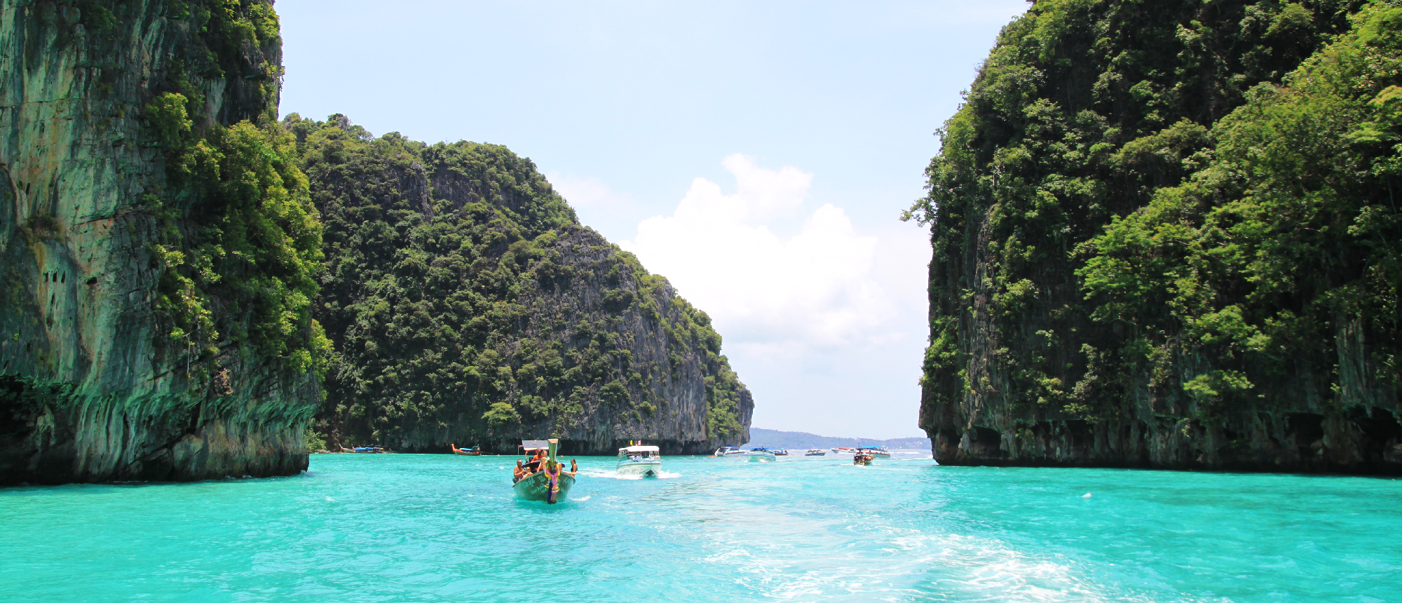Longtail boat with people navigating turquoise waters between lush, towering limestone islands in Phi Phi.