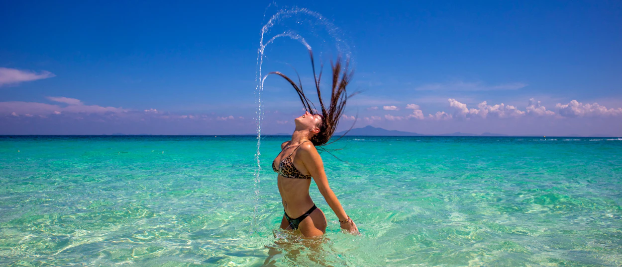 A woman joyfully flips her wet hair, splashing water in the clear turquoise sea, Phi Phi Islands.