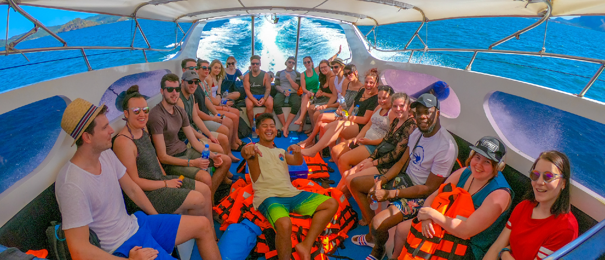 A group of smiling travelers enjoy a speed boat ride on the clear blue waters of Thailand.