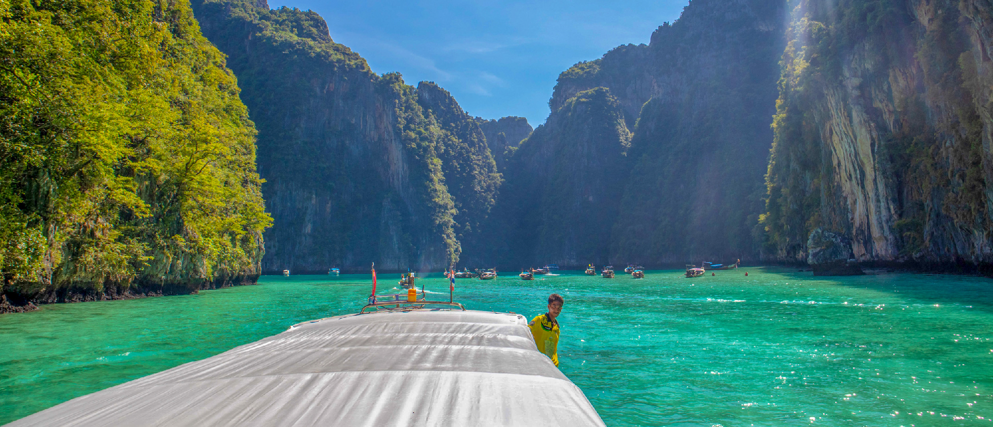 Boating through a stunning turquoise bay surrounded by towering green limestone cliffs in Phi Phi Islands.