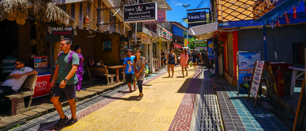 A bustling pedestrian street with shops and tourists enjoying the sunny atmosphere on Phi Phi Islands.