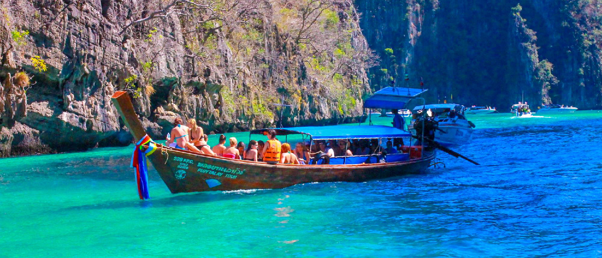 Tourists enjoy a longtail boat ride on turquoise waters surrounded by towering limestone cliffs in Krabi, Thailand.