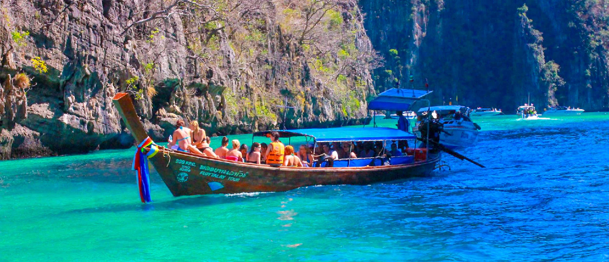 Tourists enjoy a longtail boat ride on turquoise waters surrounded by towering limestone cliffs in Krabi, Thailand.