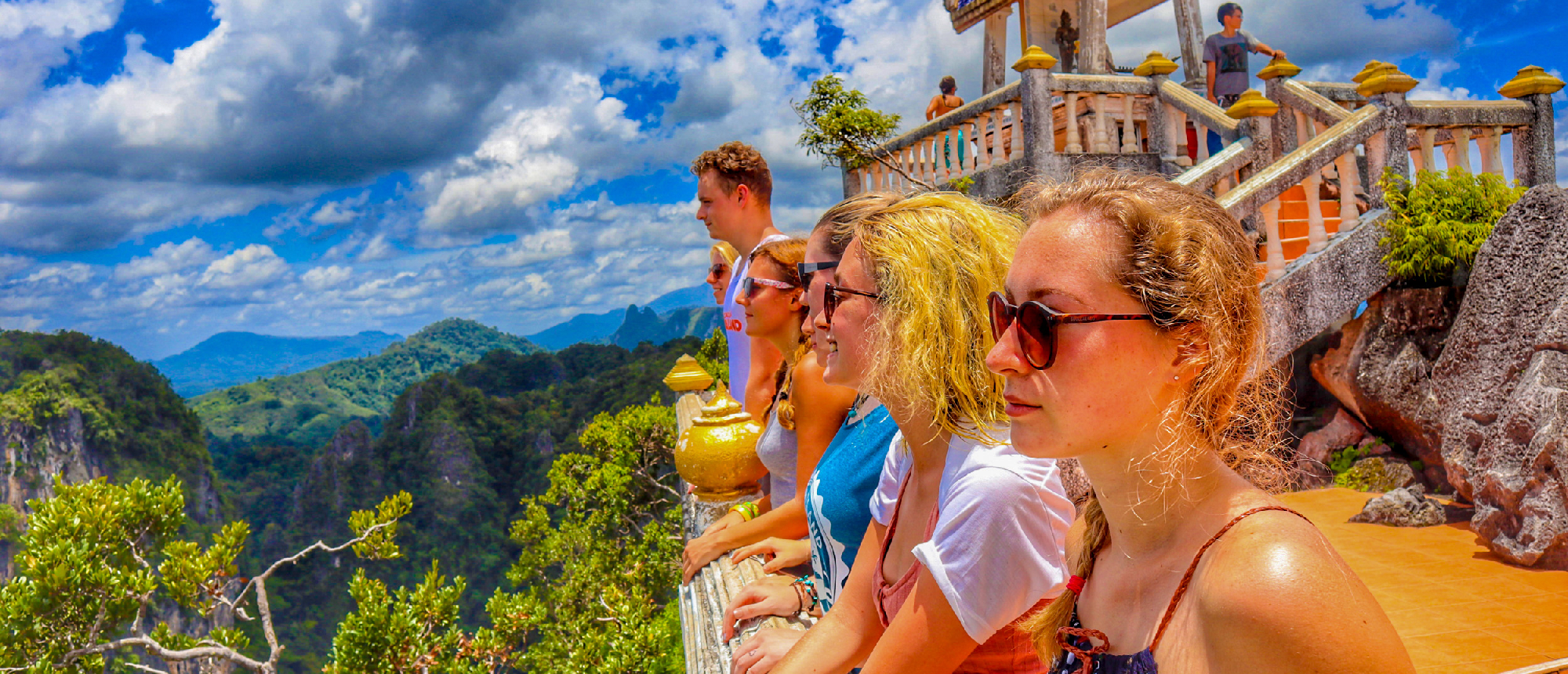 Travelers gaze at the stunning panoramic view of lush green mountains from a temple viewpoint in Krabi.