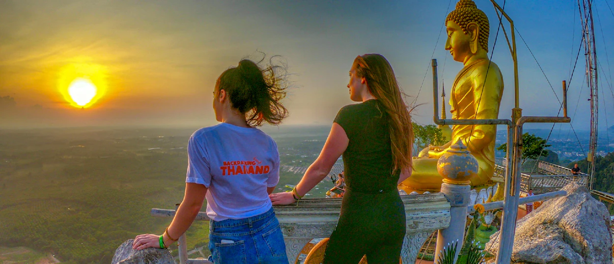Two women admire a golden sunset over a vast landscape from a temple viewpoint in Krabi.