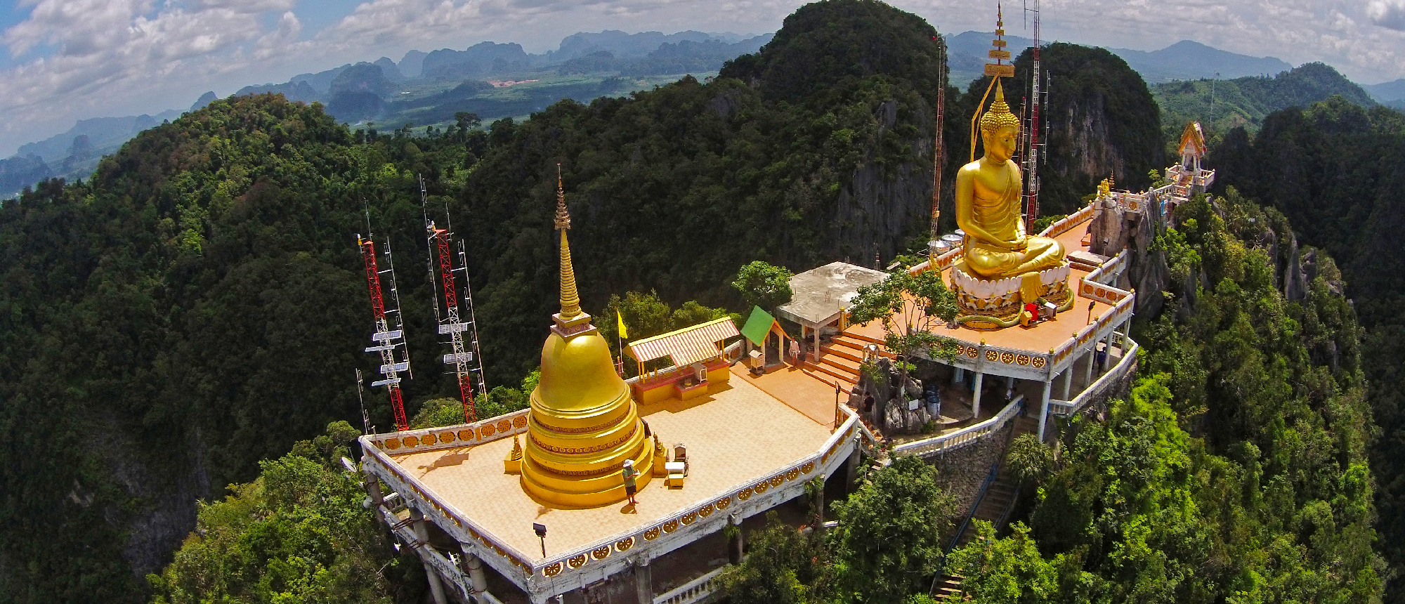 Golden Buddha statue and stupa on a mountaintop, surrounded by lush green jungle in Krabi, Thailand.