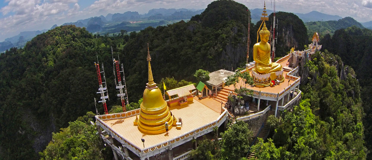 Golden Buddha statue and stupa on a mountaintop, surrounded by lush green jungle in Krabi, Thailand.