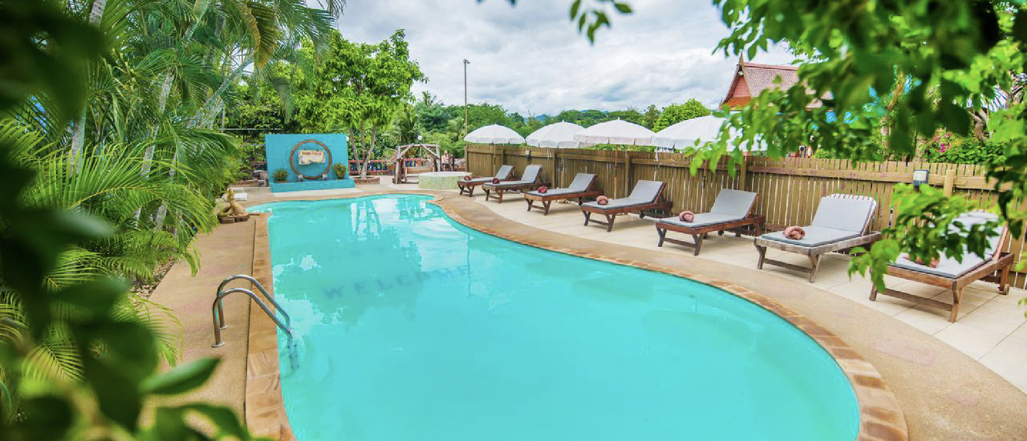 Inviting resort swimming pool with empty lounge chairs nestled among vibrant tropical foliage.