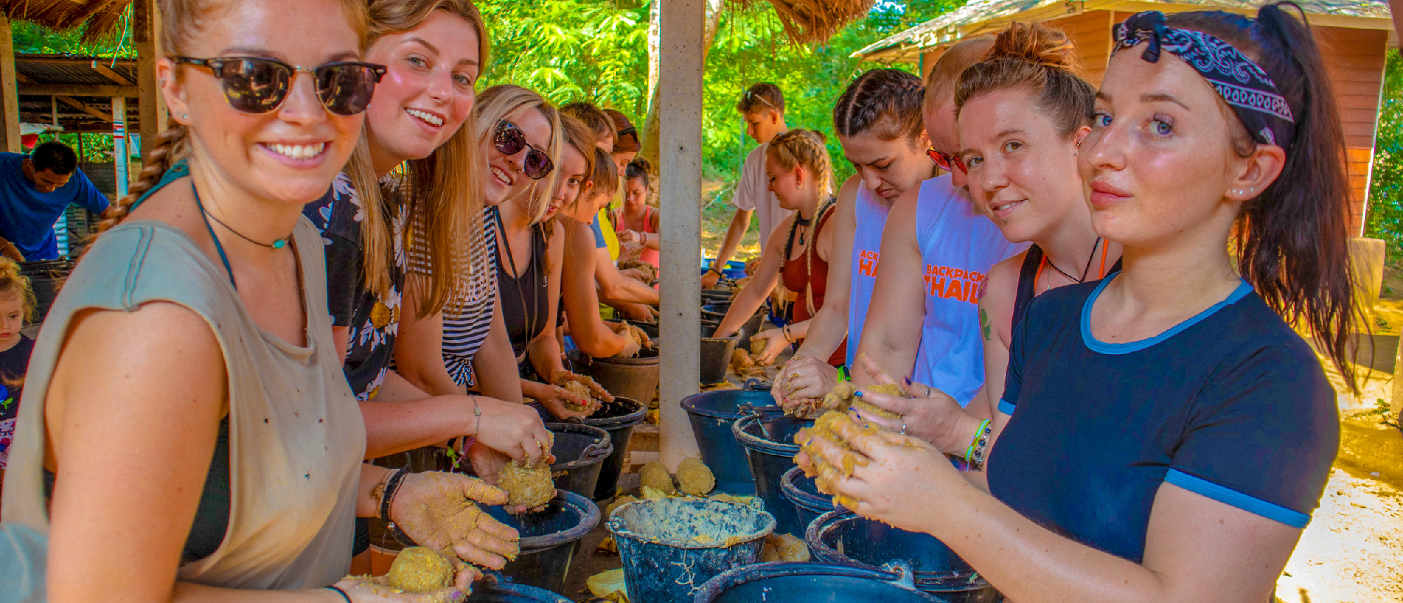 Happy travelers in Kanchanaburi preparing food for elephants at a sanctuary.