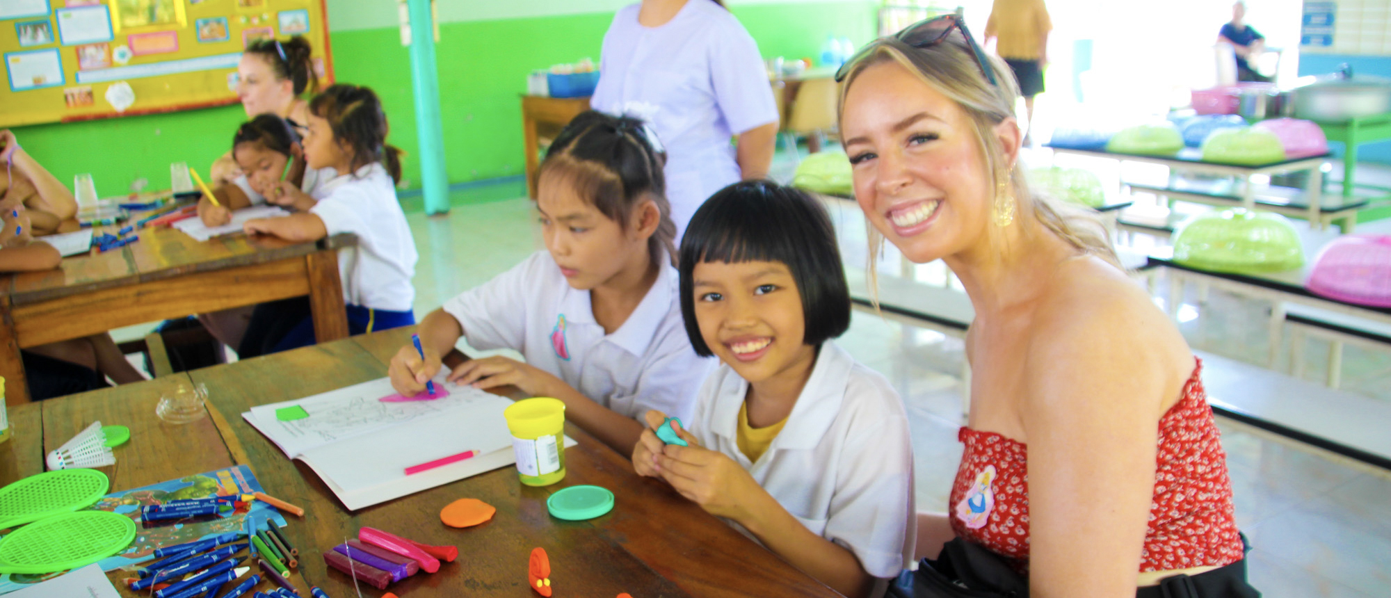 A happy tourist and two Thai schoolgirls engaging in a craft activity in Amaphawa.