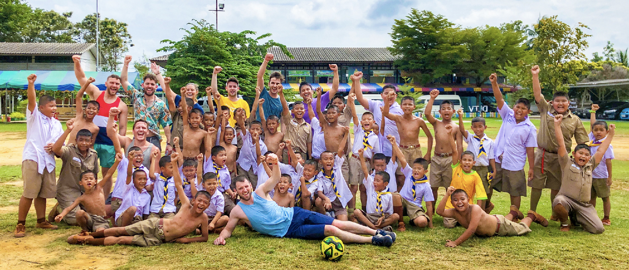 Joyful Thai students and backpackers celebrate with raised fists on a school field in Amaphawa.