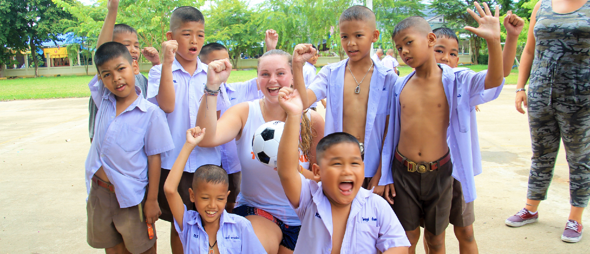 Happy Thai students and a guide cheer with a soccer ball at a school in Amaphawa.