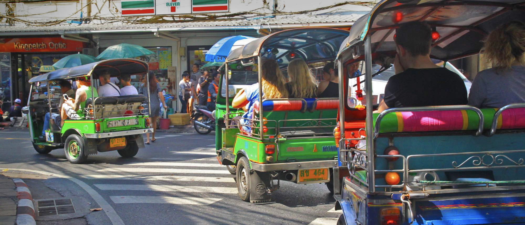 Tourists ride colorful tuk-tuks through a busy street in Bangkok, enjoying the city's vibrant atmosphere.