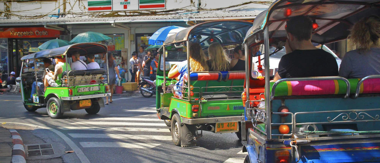Tourists ride colorful tuk-tuks through a busy street in Bangkok, enjoying the city's vibrant atmosphere.