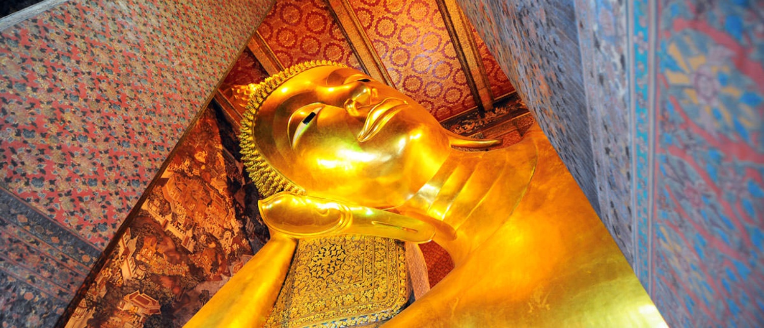 A massive golden reclining Buddha statue with a serene expression, surrounded by ornate temple walls in Bangkok.