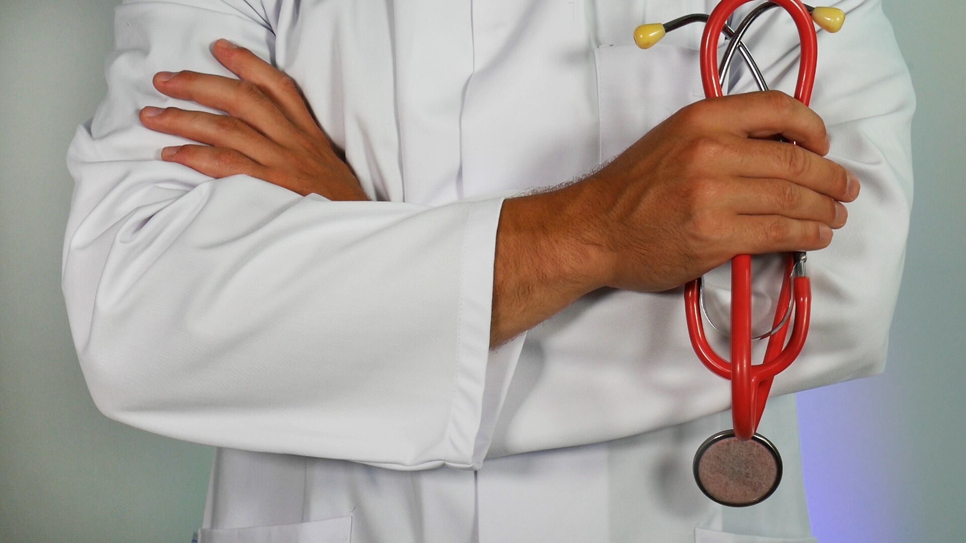 A doctor in a white coat with crossed arms, holding a red stethoscope.