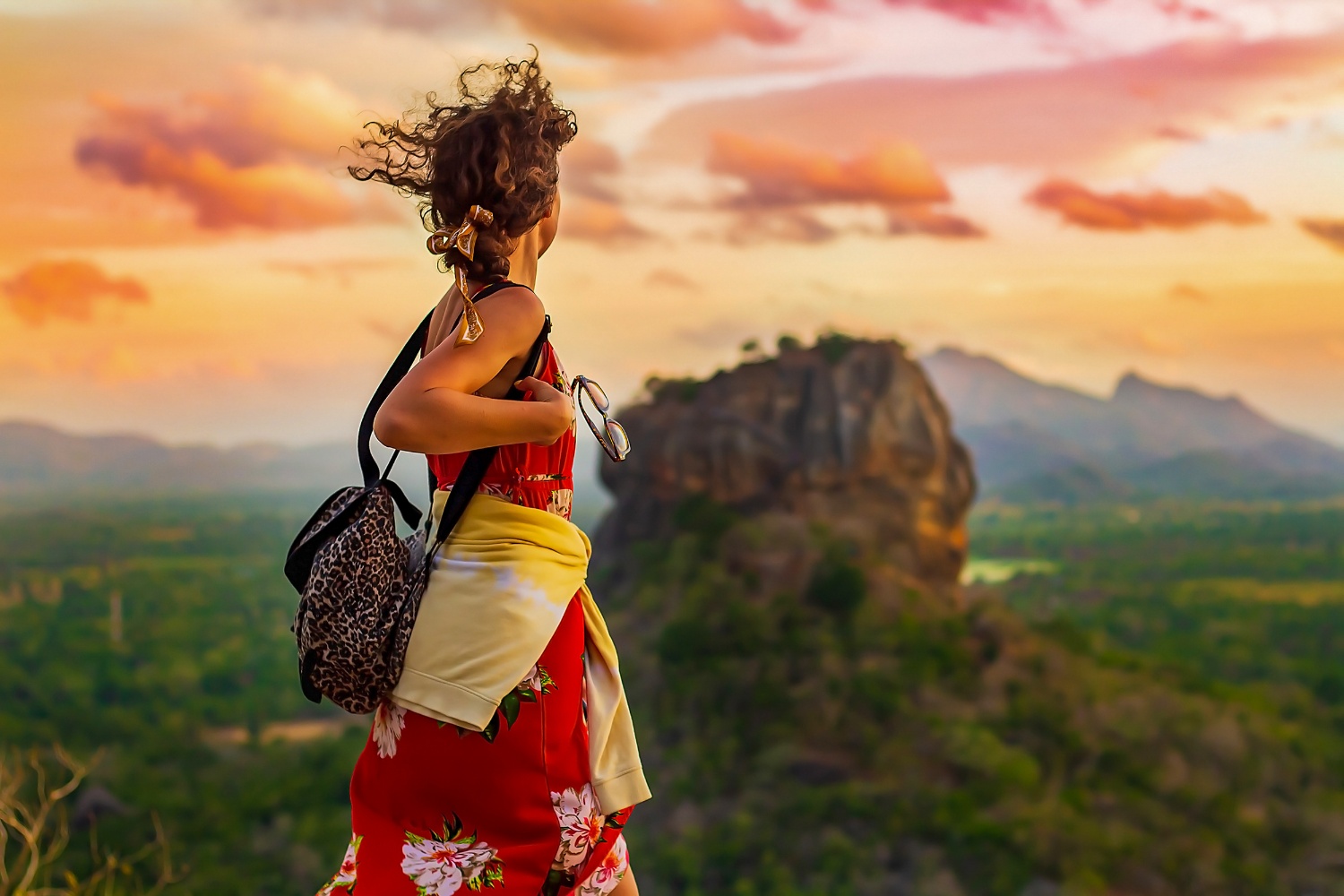 Woman with wind-blown hair gazes at the iconic Sigiriya rock at sunset in Sri Lanka.