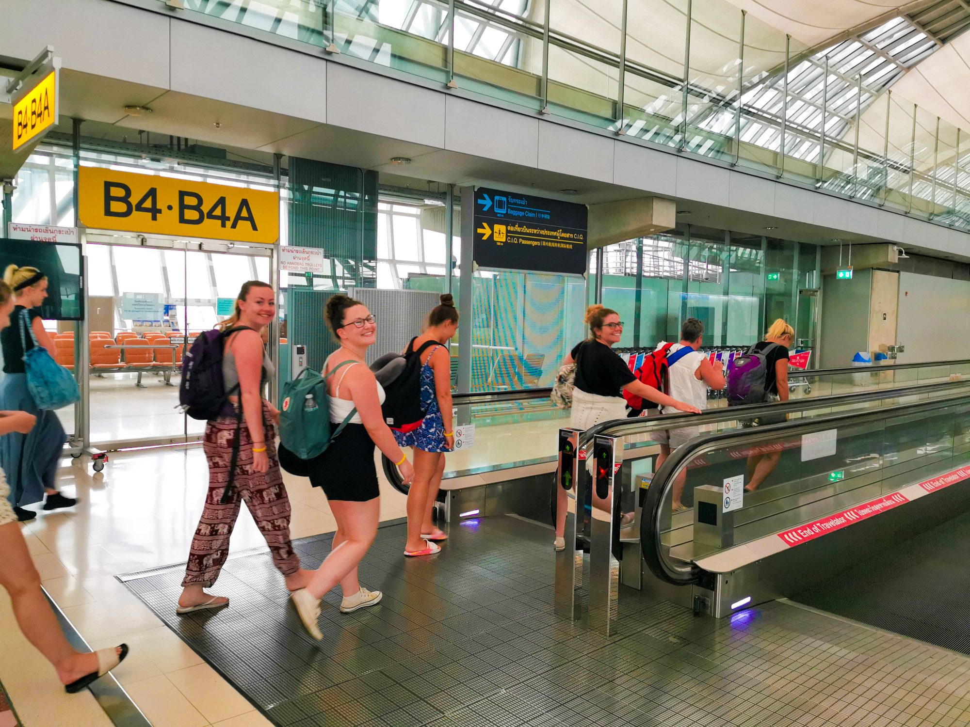 Smiling backpackers on a moving walkway in a Thai airport terminal after landing