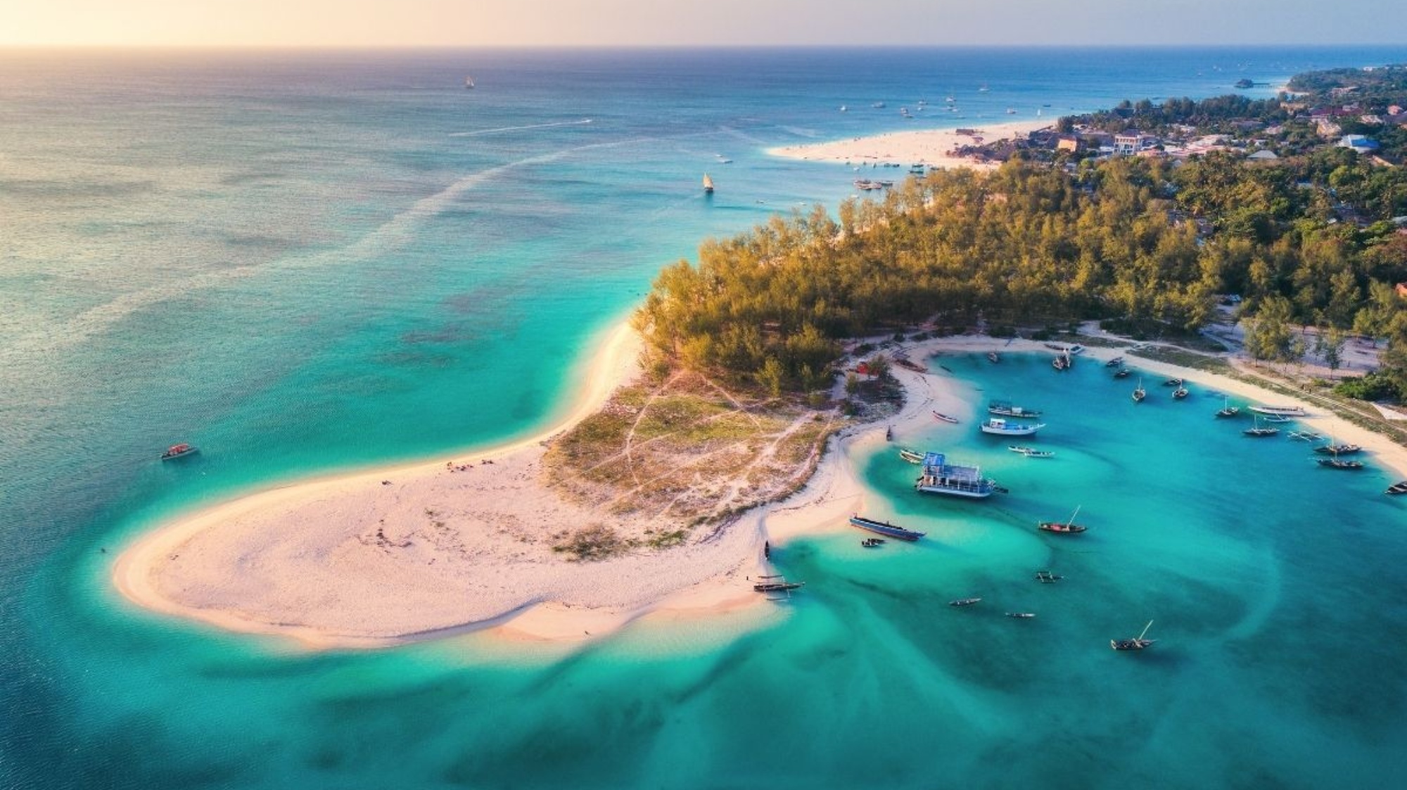 Stunning aerial view of Zanzibar's tropical coastline, featuring turquoise waters, sandy beaches, and anchored boats.