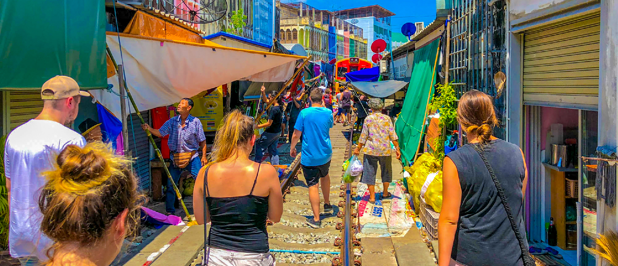 Tourists walk along train tracks lined with colorful market stalls at Amphawa.