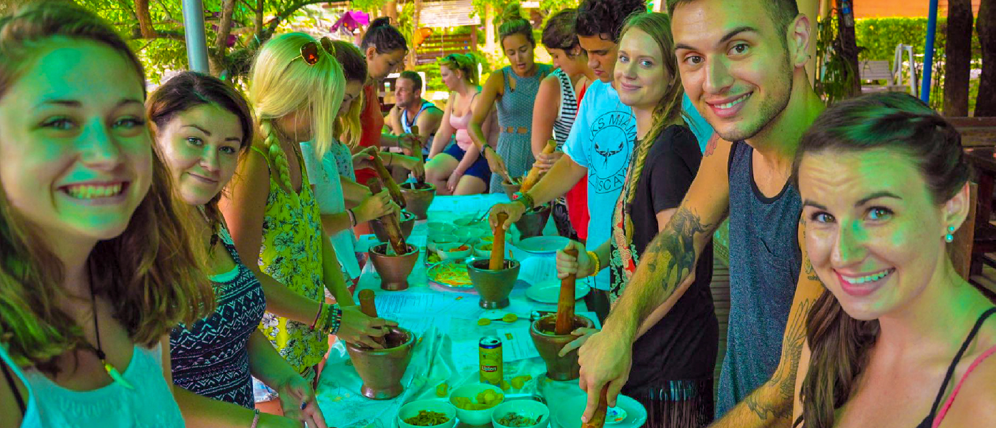Smiling backpackers learn to cook Thai dishes using mortars and pestles during a class in Amaphawa.