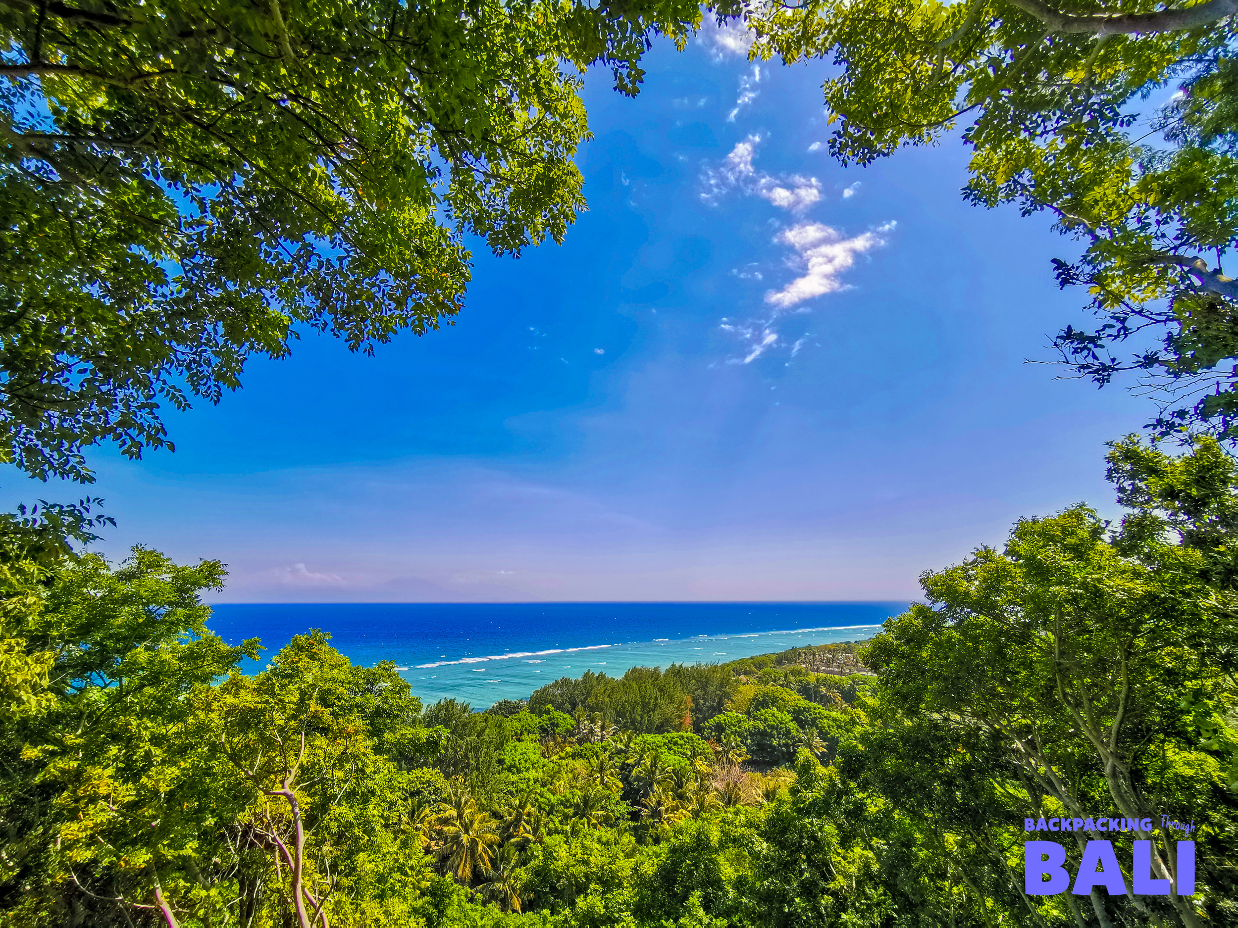 Lush green tropical trees frame a vibrant blue ocean and coastline view on Gili Trawangan.