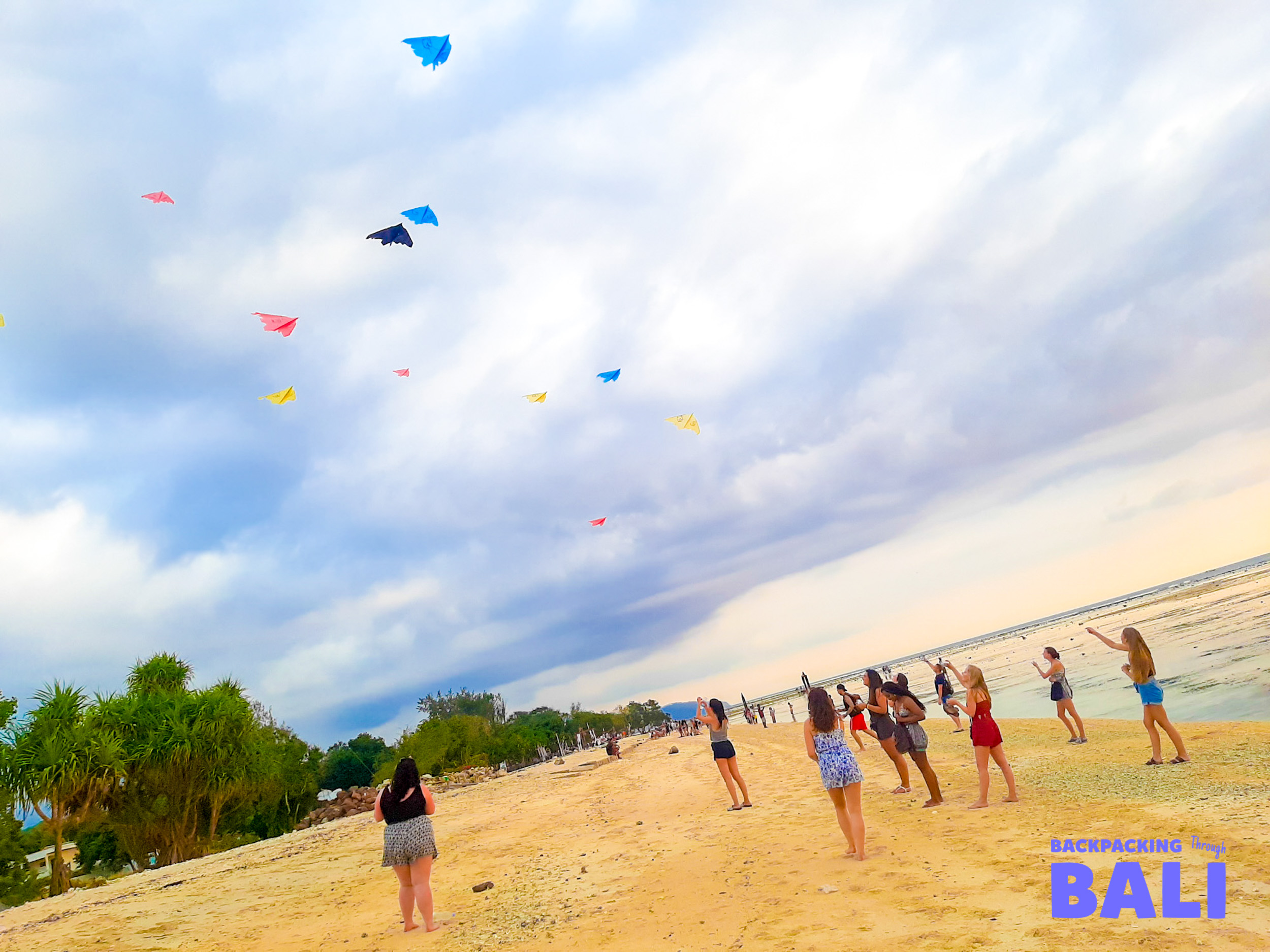 Colorful kites soar above people enjoying the sandy beach and clear waters of Gili Trawangan.