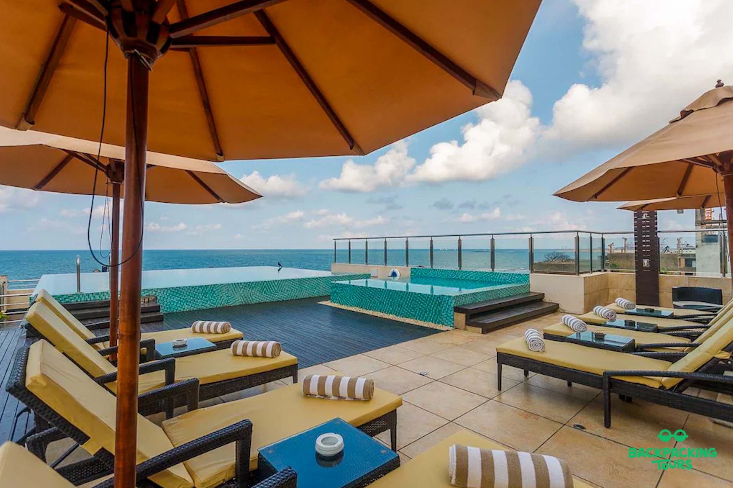 Rooftop infinity pool and sun loungers with ocean views under a blue sky in Colombo.