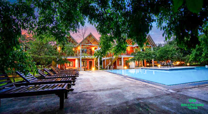 Tropical resort with a swimming pool and lounge chairs, framed by green trees in Dambulla, Sri Lanka.