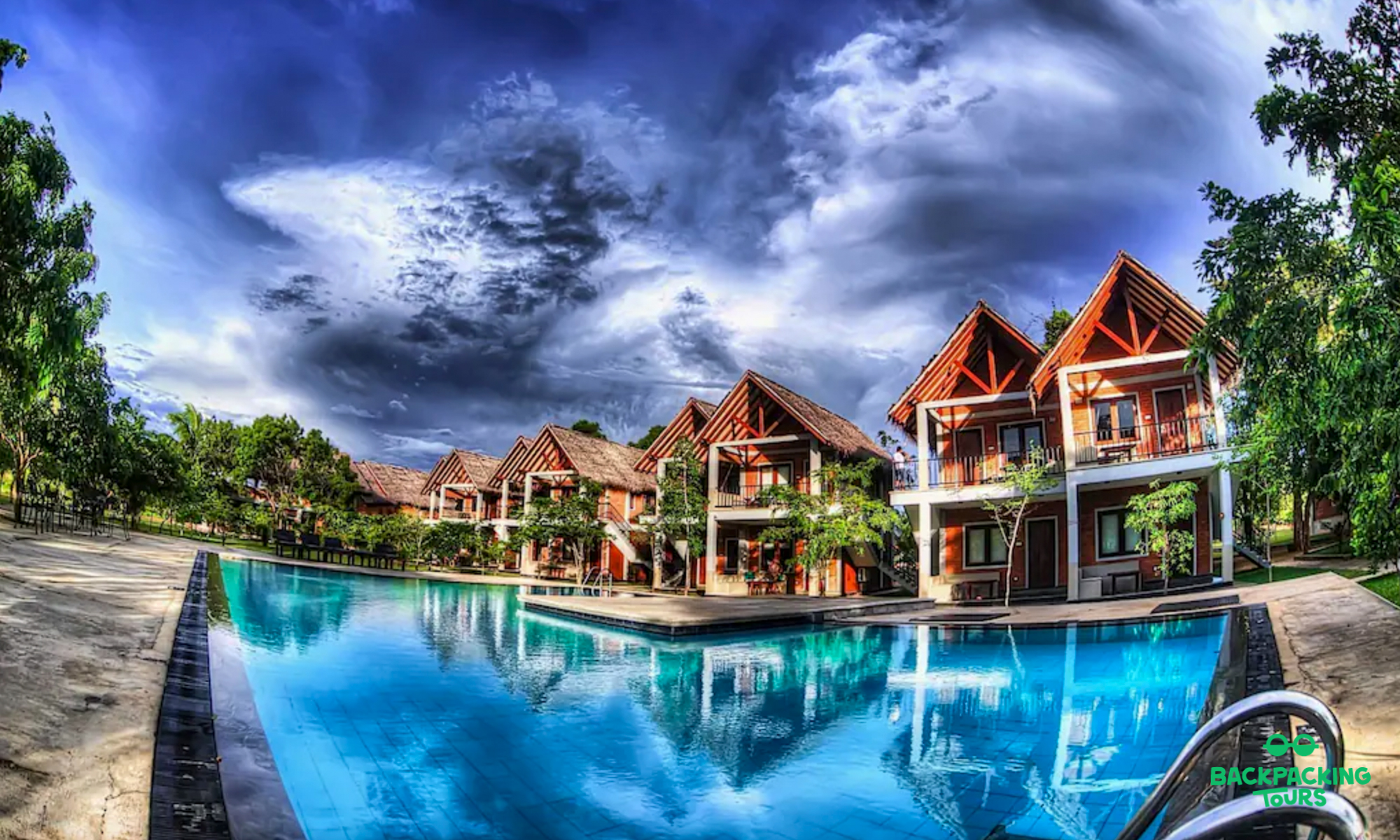 Modern bungalows with red roofs and balconies reflected in a large blue swimming pool in Dambulla.
