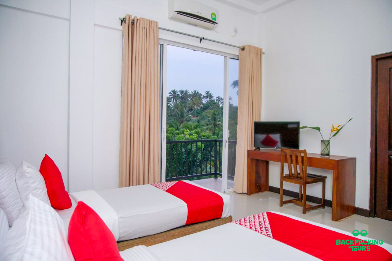 A clean and bright twin room with a balcony overlooking tropical greenery in Sri Lanka.