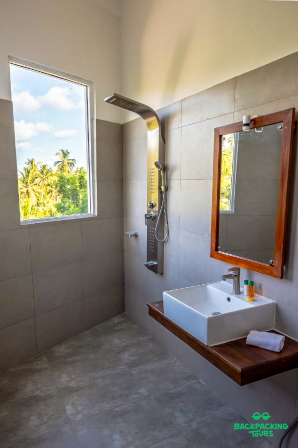 Modern bathroom with a large window overlooking tropical palm trees, featuring a stylish shower and sink.
