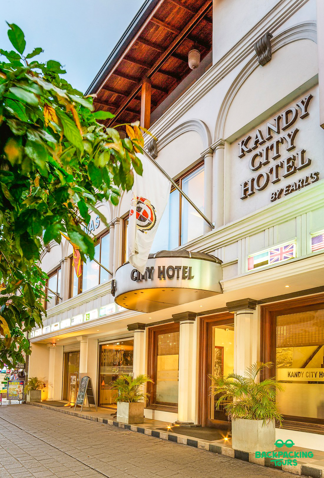 The modern exterior of Kandy City Hotel with lush green plants and national flags.
