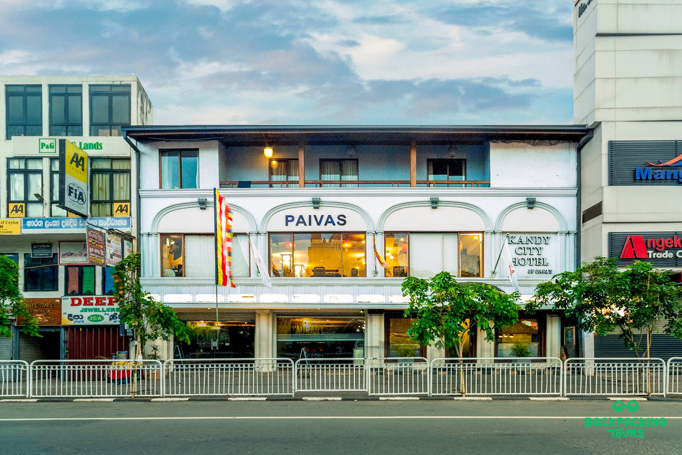 A white multi-story building with 'Paivas' and 'Kandy City Hotel' signs on a bustling city street.