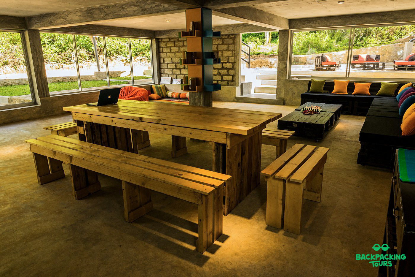 A spacious and inviting common room in Ella with wooden tables, benches, and comfortable sofas.