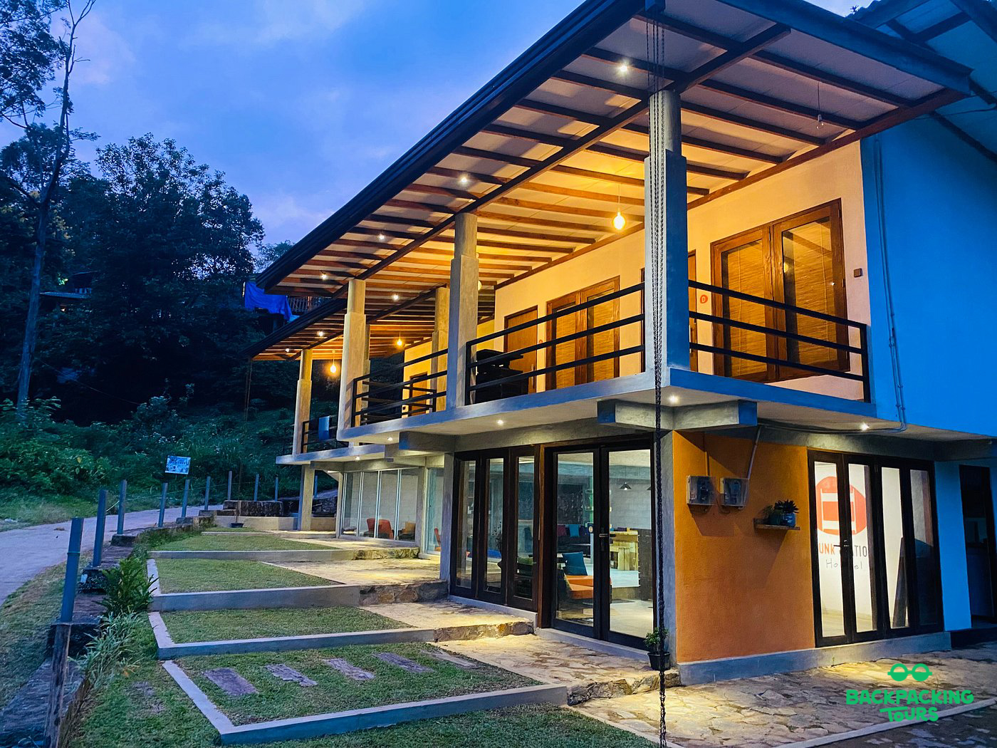 Modern guesthouse in Ella with warm lights illuminating its balconies and inviting rooms at twilight.