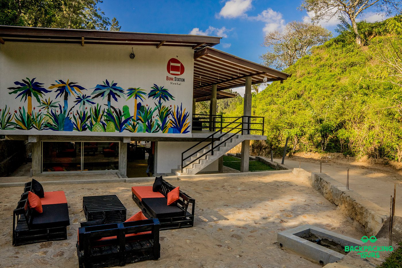 Modern accommodation with a vibrant palm tree mural and outdoor lounge seating in the lush hills of Ella.