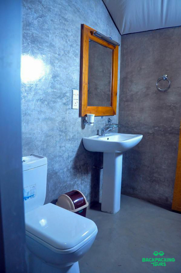 A modern bathroom with a fabric ceiling, toilet, pedestal sink, and wooden mirror in Weligama.