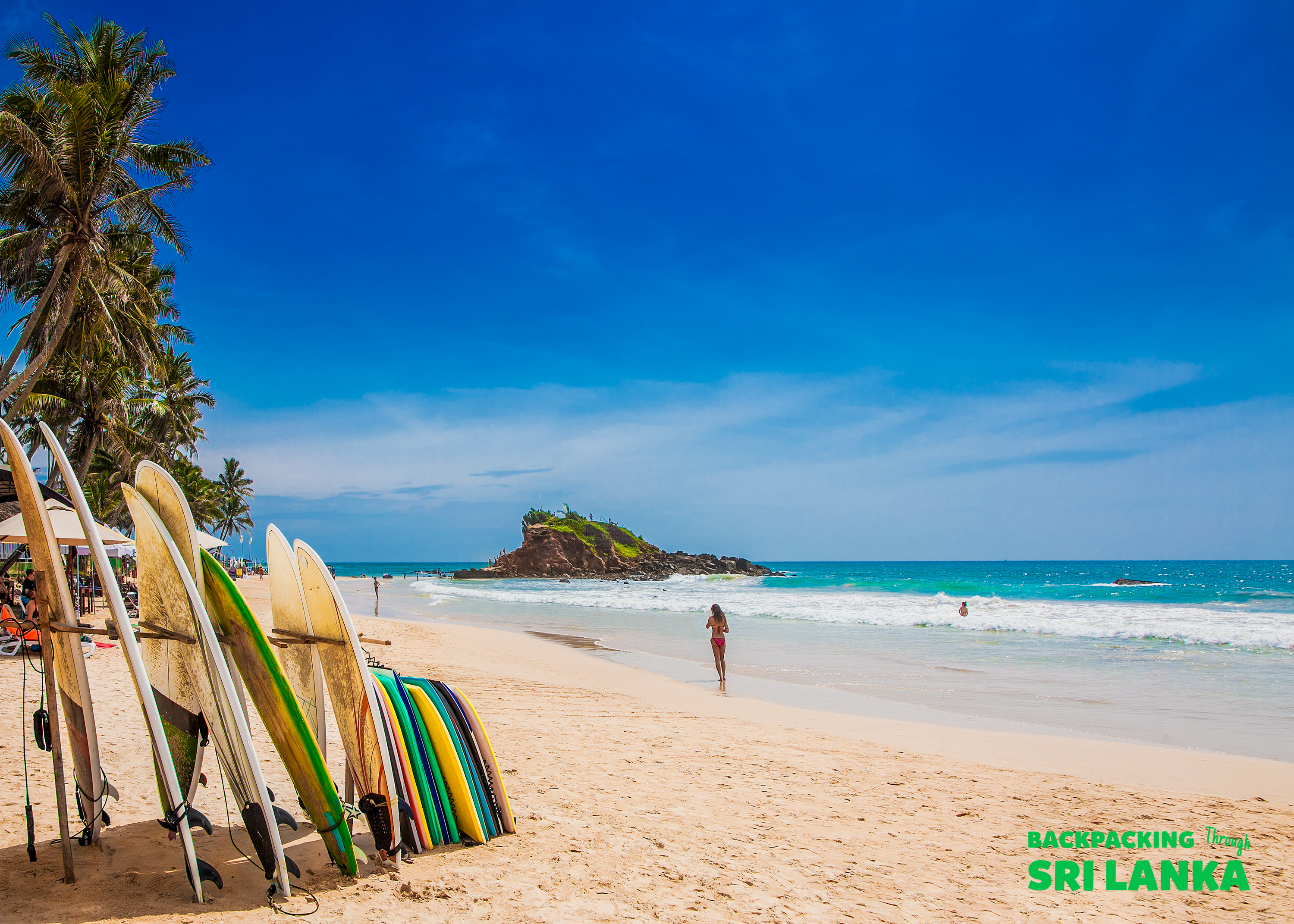 Surfboards ready for action on the sunny Weligama Beach, with a person enjoying the tropical waters.